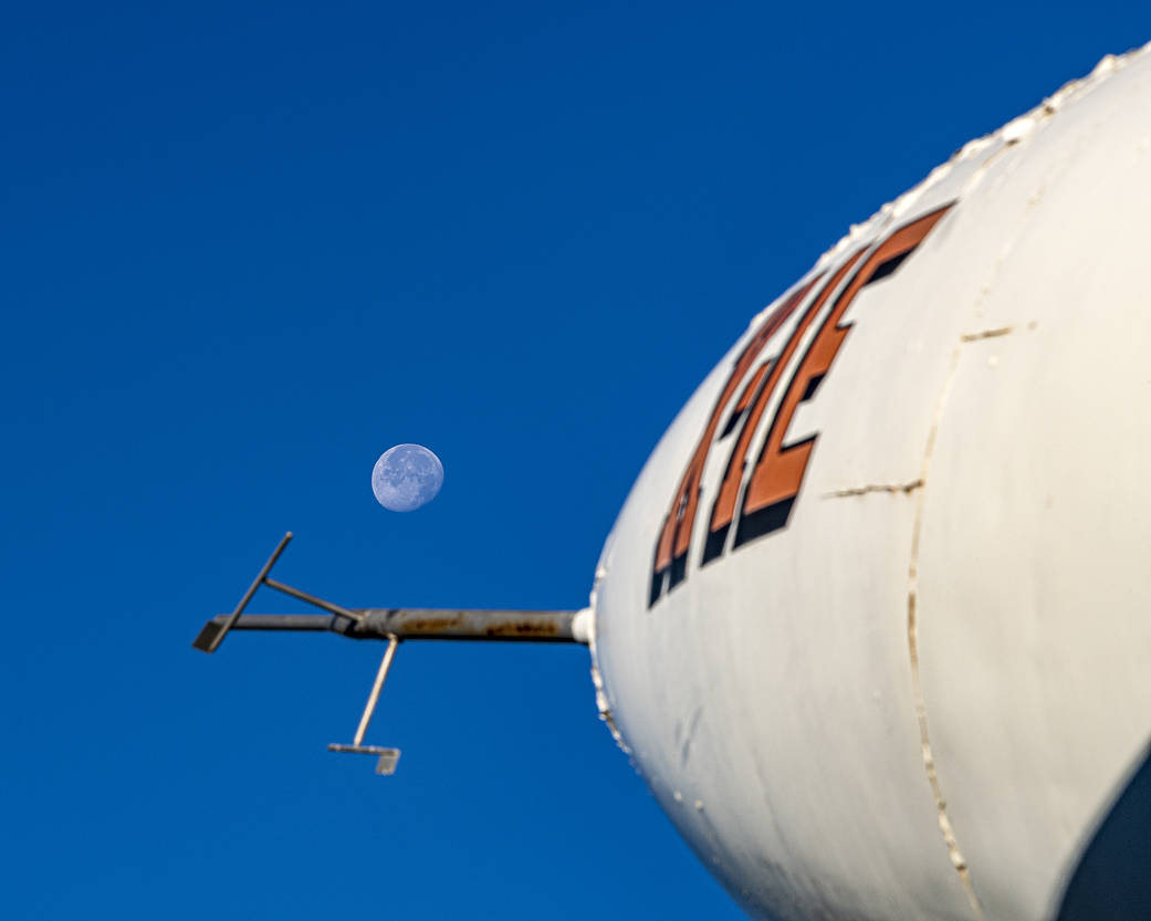 The X-1E aircraft dominates the foreground of this photo. It is white, with its designation written on its side in big orange letters. The Moon is ...